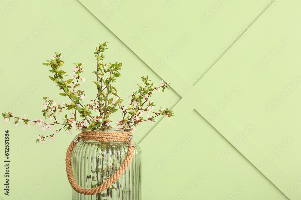 Vase with blooming tree branches on green background