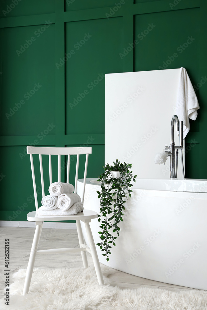 Chair with rolled towels and bathtub in interior of bathroom