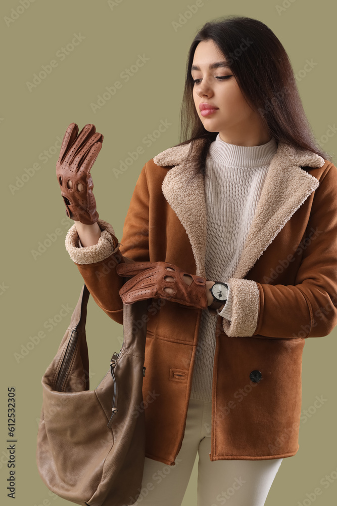 Stylish young woman in leather gloves with bag on green background