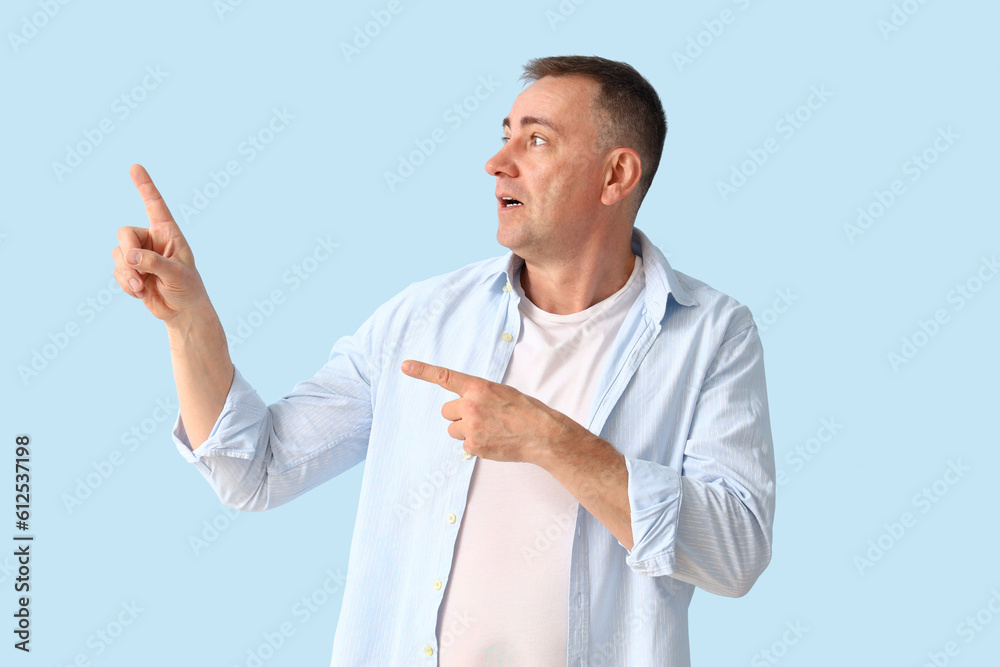 Shocked mature man pointing at something on blue background