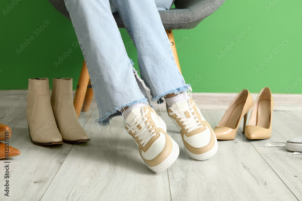 Woman in stylish sneakers sitting near color wall, closeup