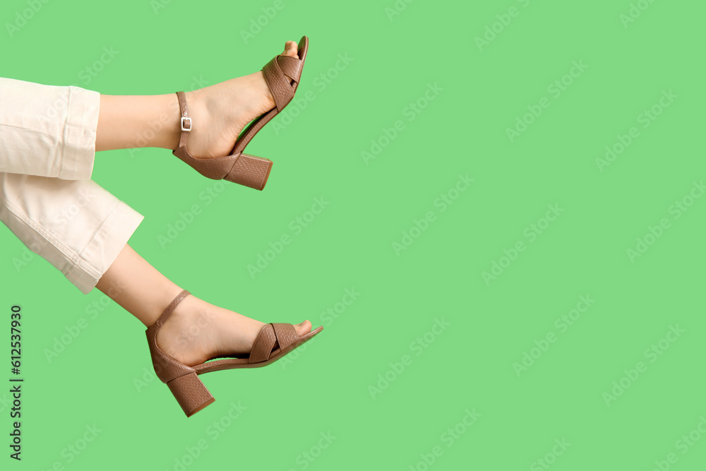 Female legs in stylish shoes on green background