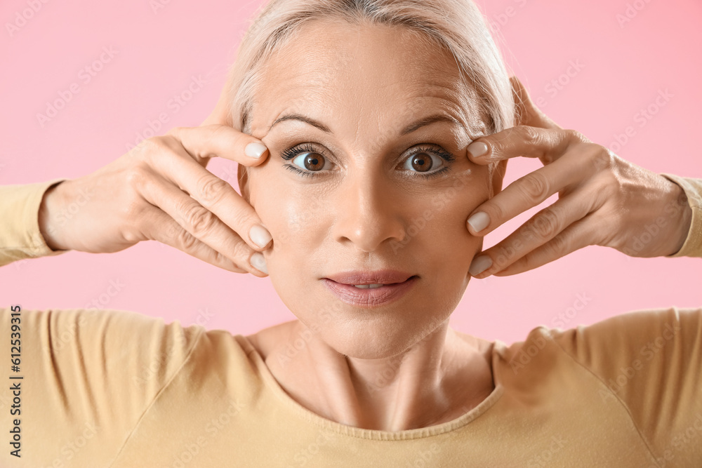 Mature woman doing face building exercise on pink background, closeup