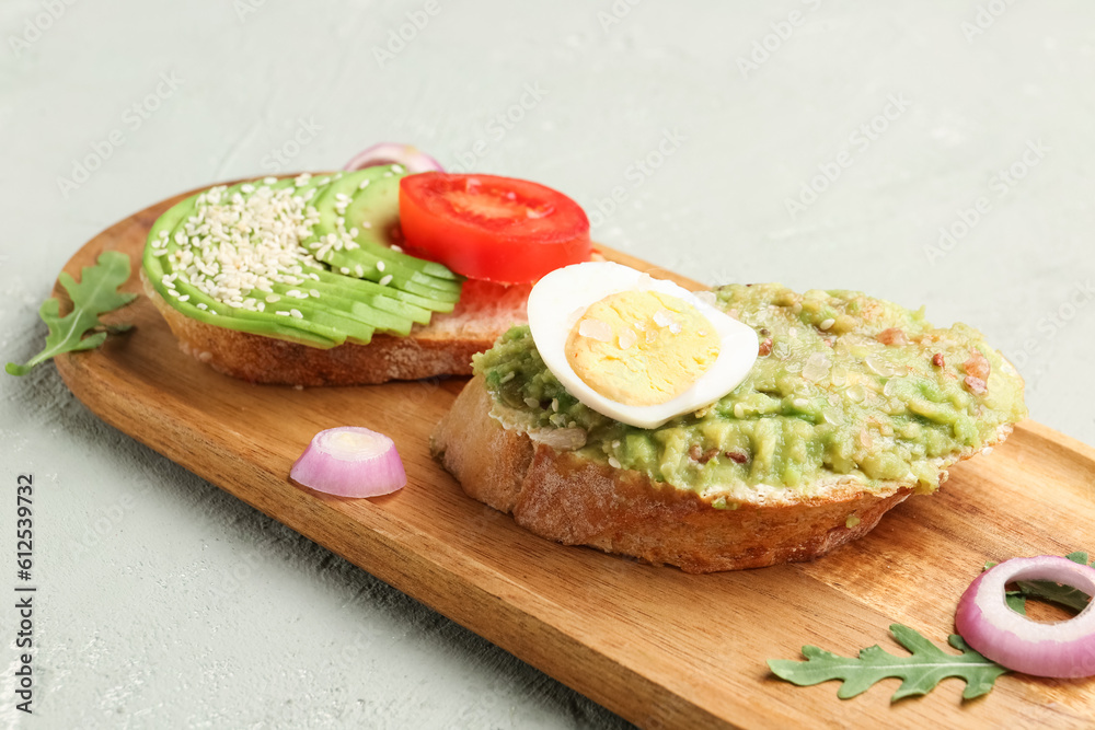 Wooden board of tasty bruschettas with avocado on light background, closeup