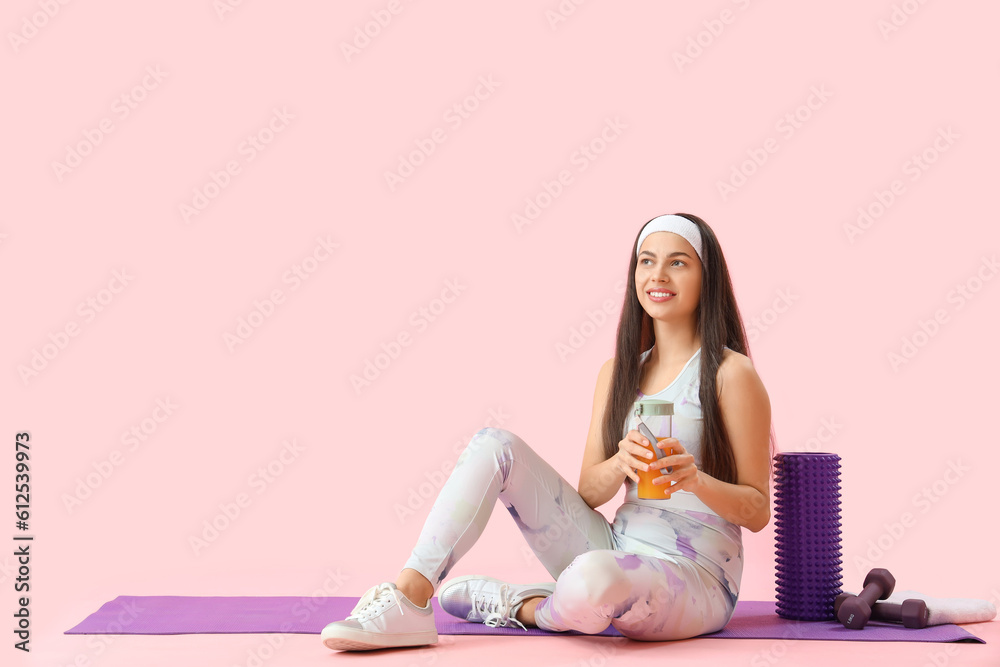 Sporty young woman with glass of vegetable juice and equipment on pink background