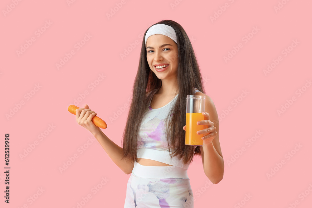 Sporty young woman with glass of vegetable juice and carrot on pink background