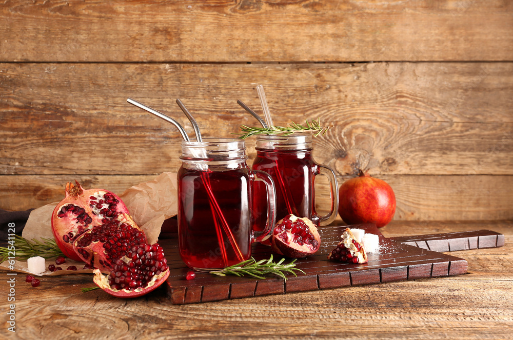 Board with mason jars of fresh pomegranate juice on brown wooden background