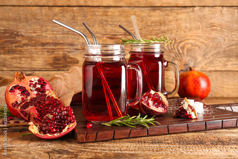 Board with mason jars of fresh pomegranate juice on brown wooden background