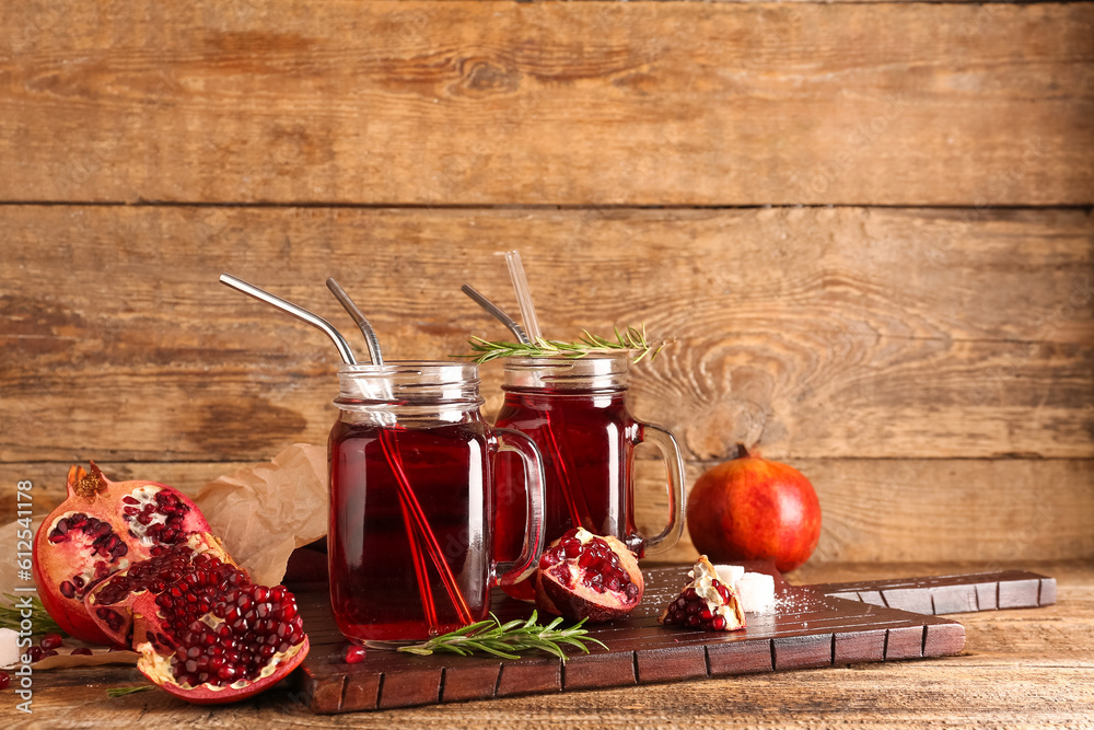 Board with mason jars of fresh pomegranate juice on brown wooden background