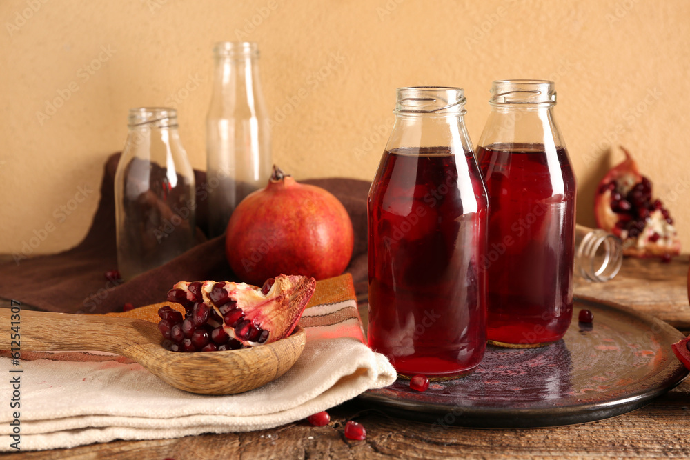 Spoon with fresh pomegranate and bottles of juice on brown wooden table