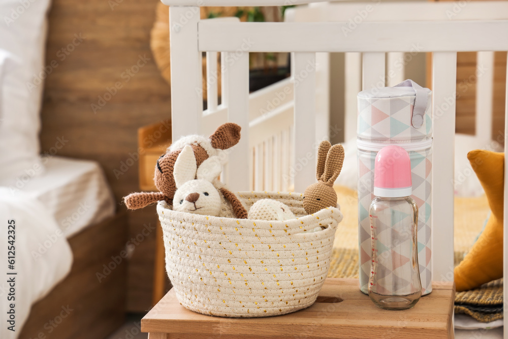 Baby bottle with toys on stool in bedroom, closeup