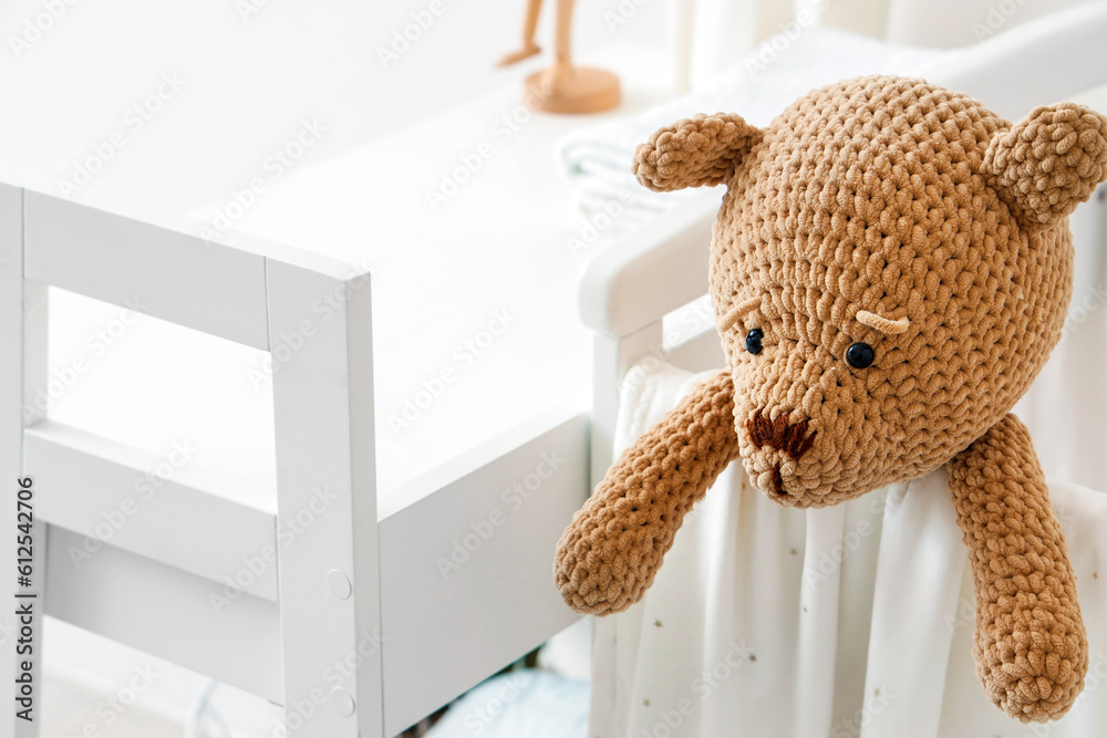 Baby crib with toy bear in light bedroom, closeup