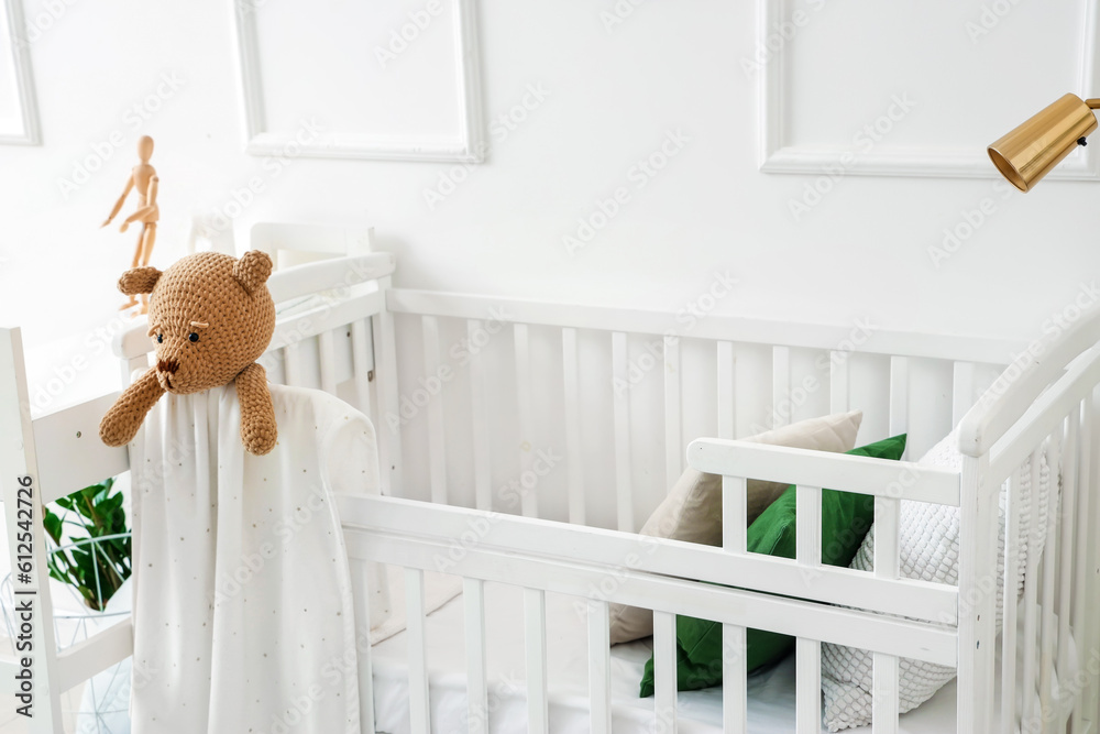 Baby crib with toy bear in light bedroom