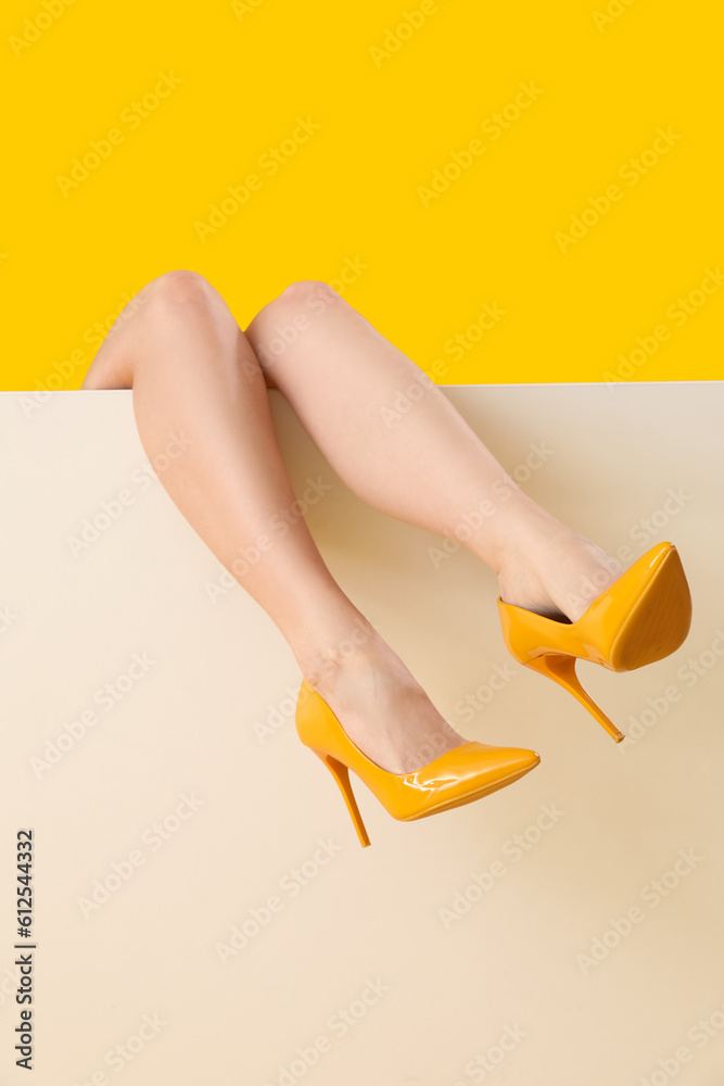 Female legs in stylish high heels on yellow background