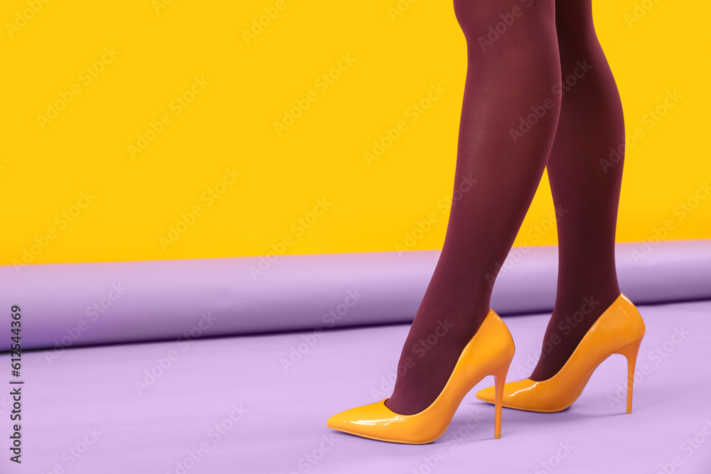 Female legs in black tights and yellow high heels on color background