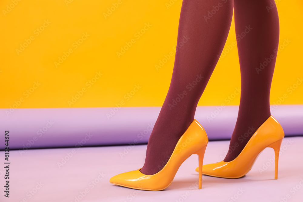 Female legs in black tights and yellow high heels on color background