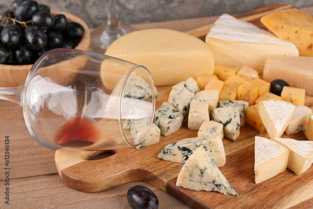 Wooden board with pieces of tasty cheese and wine glass on table