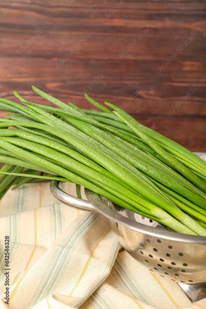 Colander with fresh green onion on wooden background