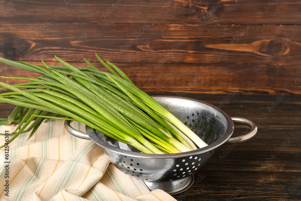 Colander with fresh green onion on wooden background