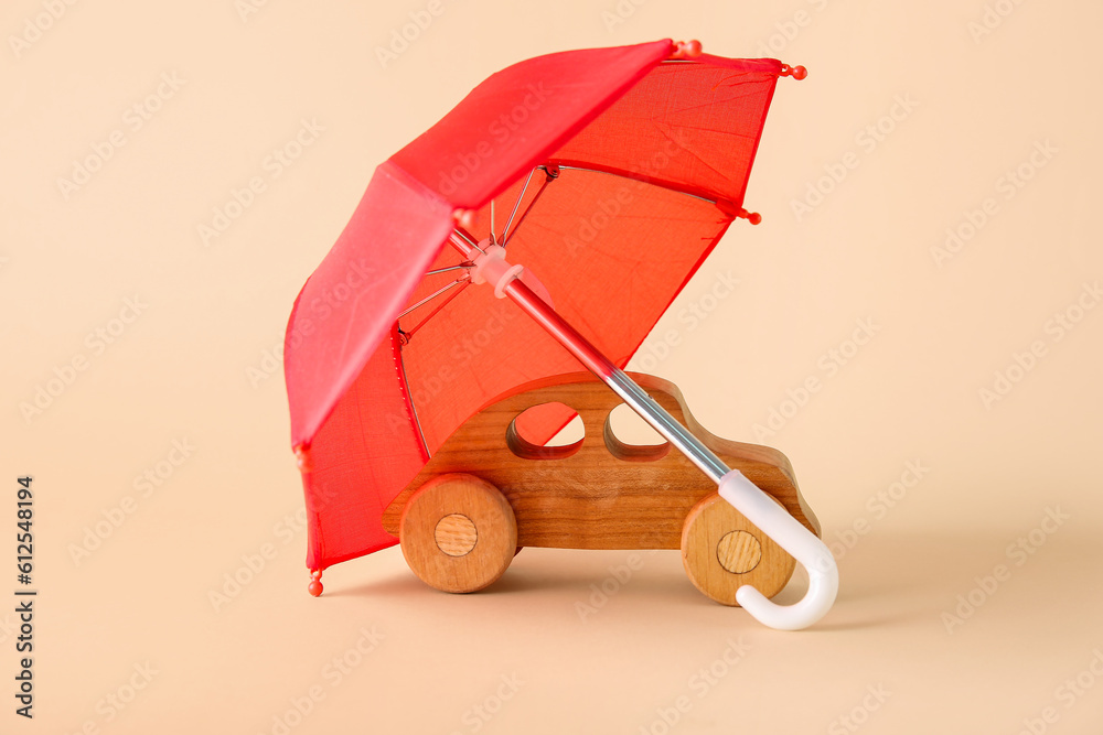 Creative composition with wooden toy car and mini umbrella on beige background. Insurance concept