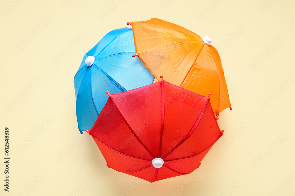 Different mini umbrellas on pale yellow background