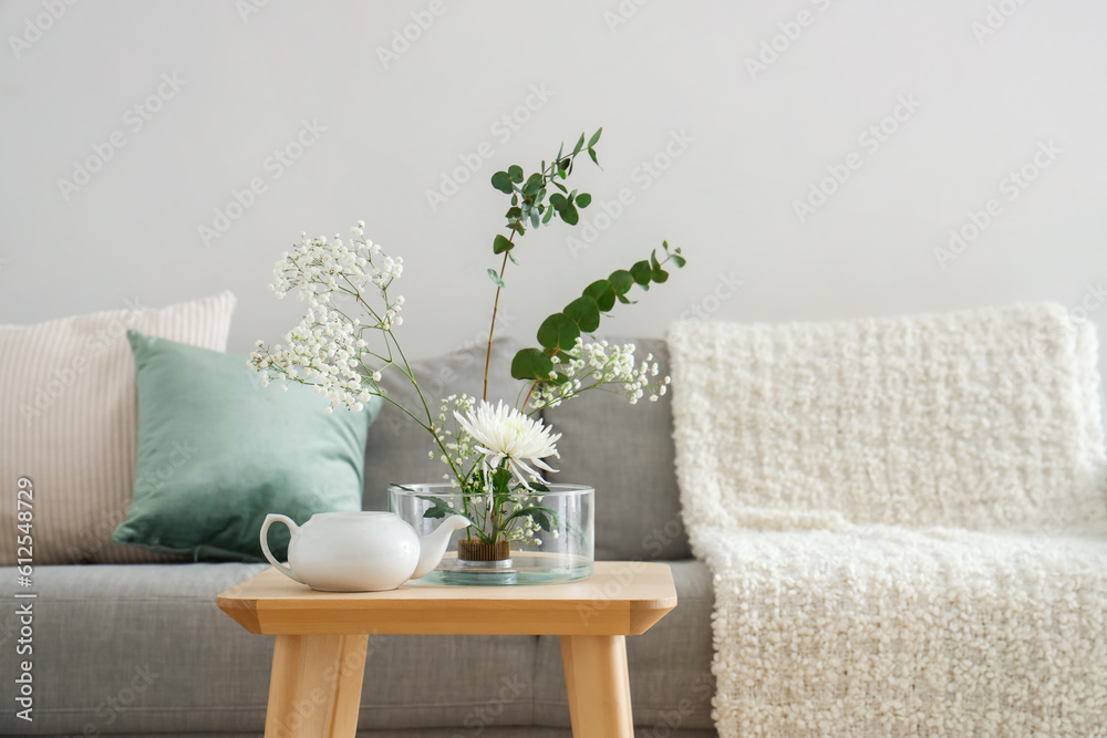 Beautiful ikebana with teapot on table in living room