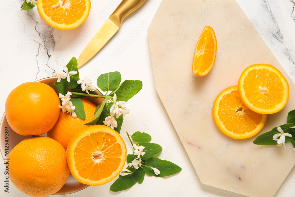 Board and bowl of oranges with blooming branches on white table