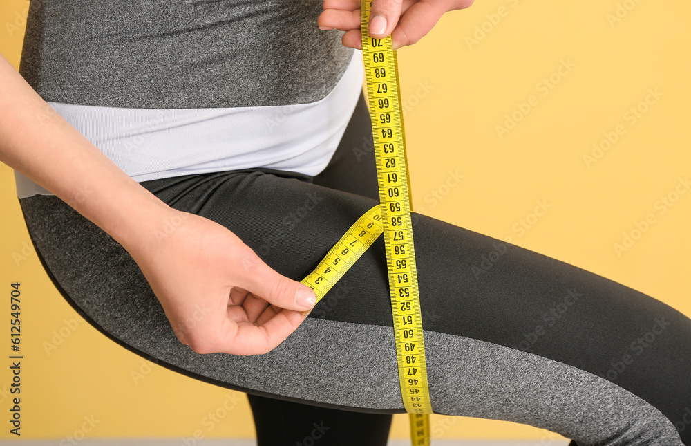 Young woman with measuring tape on beige background, closeup. Diet concept