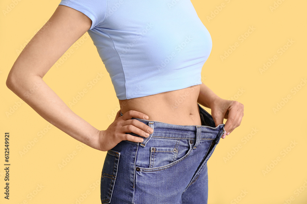 Young woman in loose jeans on beige background. Diet concept