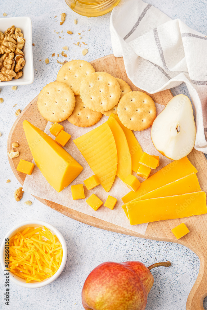 Board with tasty cheddar cheese, pear, crackers and nuts on light background