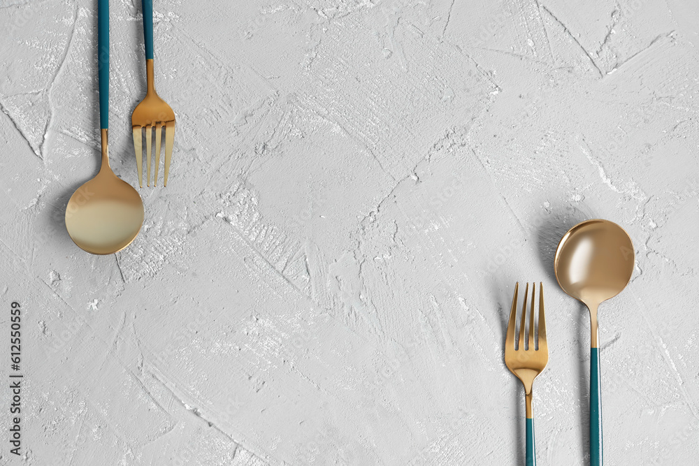 Golden spoons and forks with blue handles on grey background