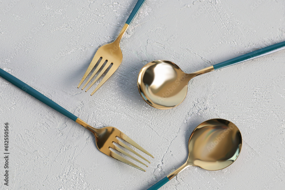 Golden spoons and forks with blue handles on grey background