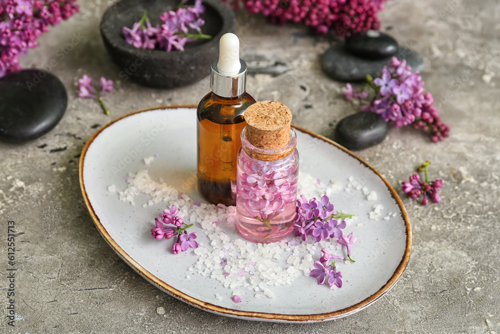 Bottles of cosmetic oil with beautiful lilac flowers and sea salt on grey table