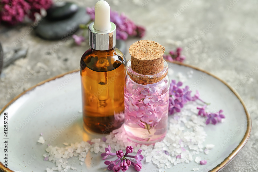 Bottles of cosmetic oil with beautiful lilac flowers and sea salt on grey table