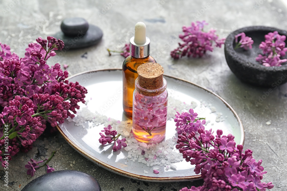 Bottles of cosmetic oil with beautiful lilac flowers and sea salt on grey table