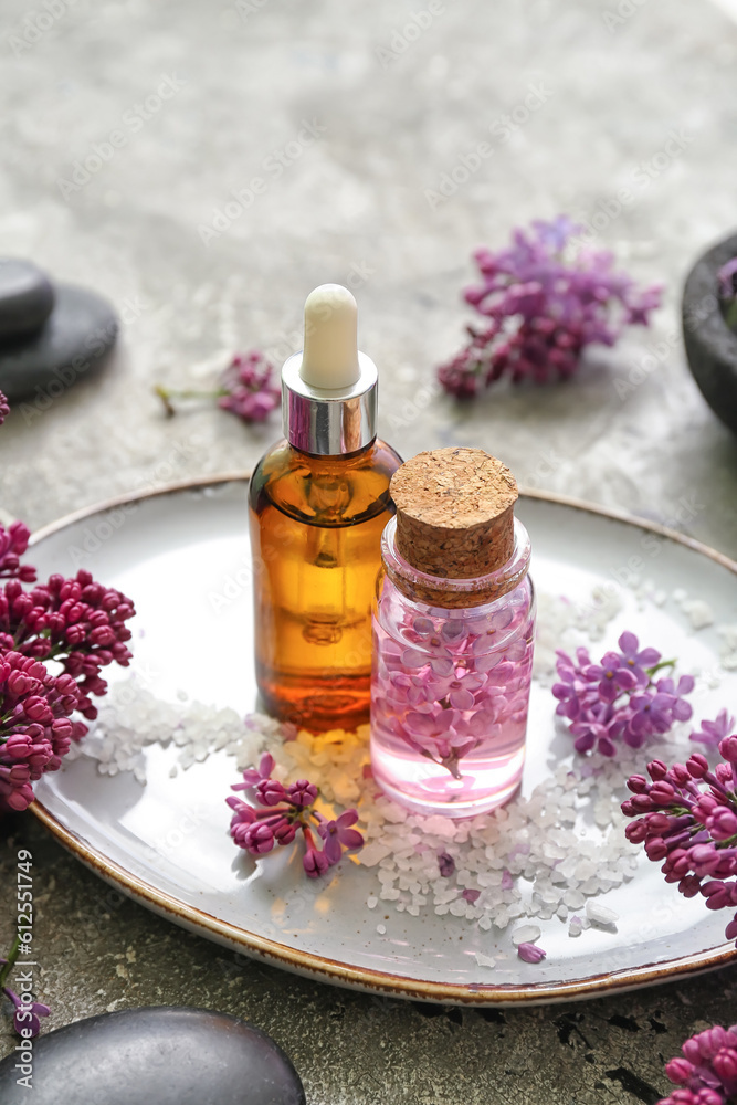 Bottles of cosmetic oil with beautiful lilac flowers and sea salt on grey table