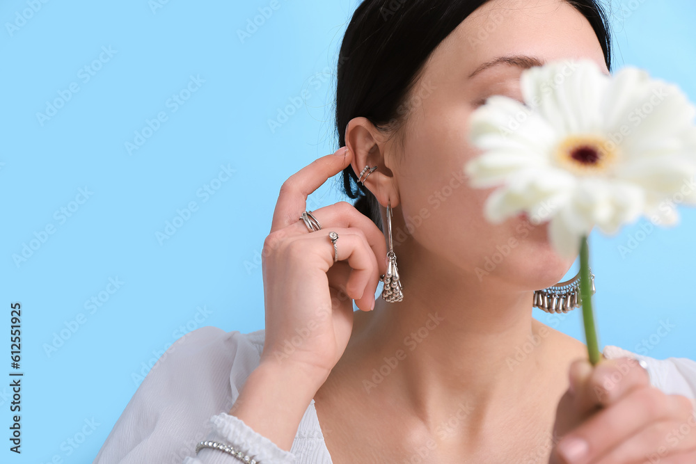 Beautiful woman with stylish jewelry and flower near blue wall