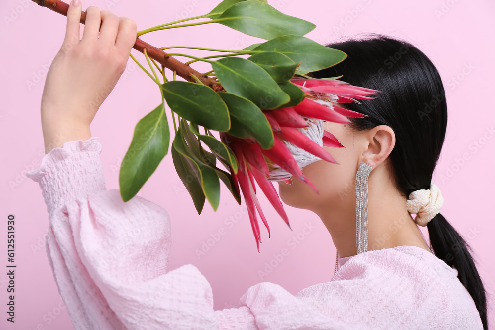 Profile of beautiful young woman wearing stylish earrings with protea flower near pink wall