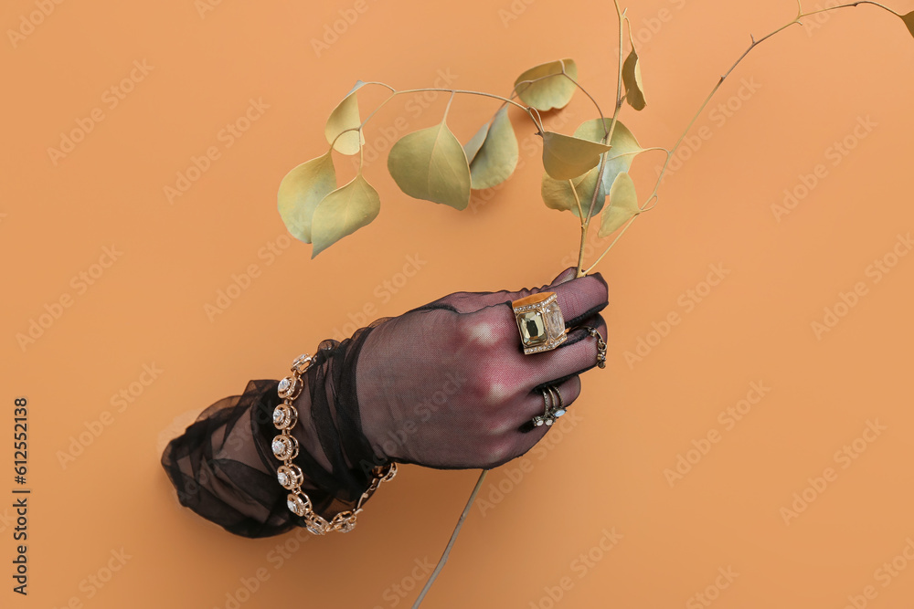 Hand of young woman in gloves wearing stylish jewelry visible through torn orange paper