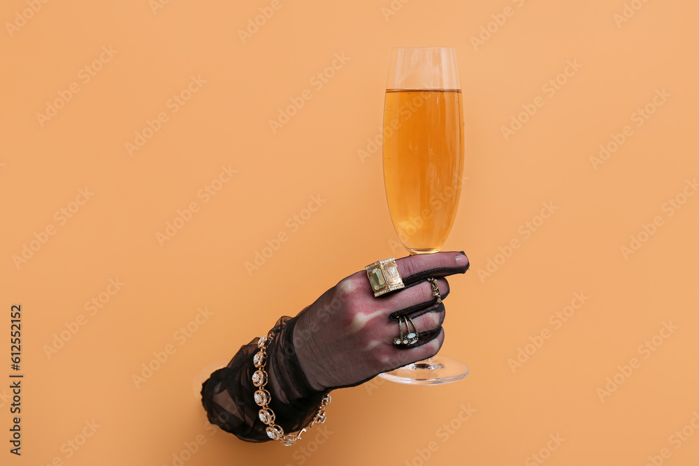 Hand of young woman in gloves wearing stylish jewelry with champagne visible through torn orange pap