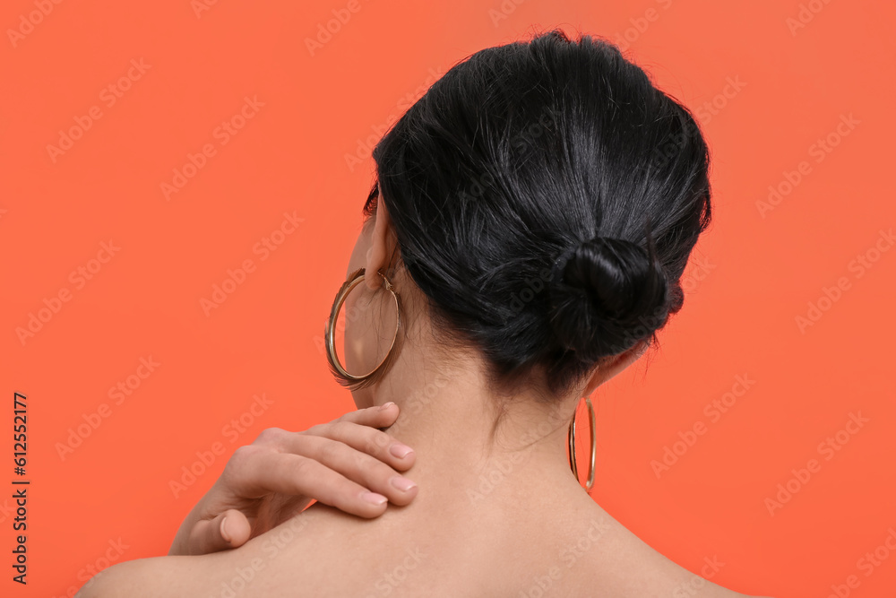 Beautiful young woman wearing stylish earrings near orange wall, back view