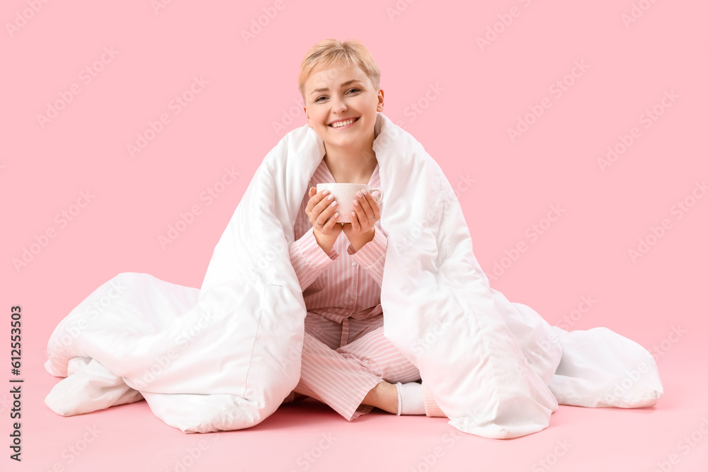 Young woman with cup of coffee and blanket sitting on pink background