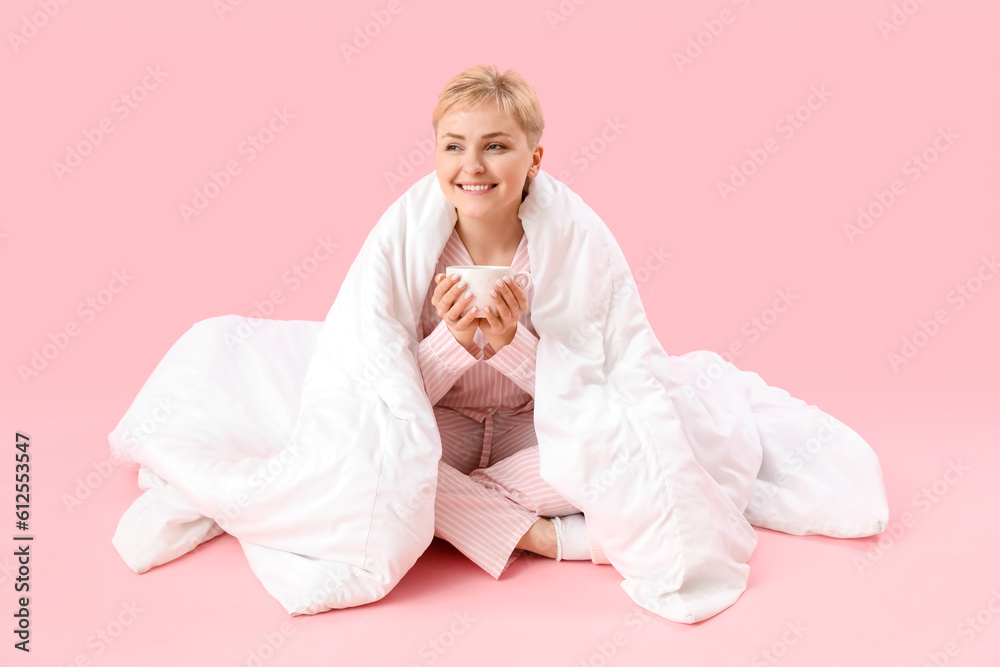 Young woman with cup of coffee and blanket sitting on pink background