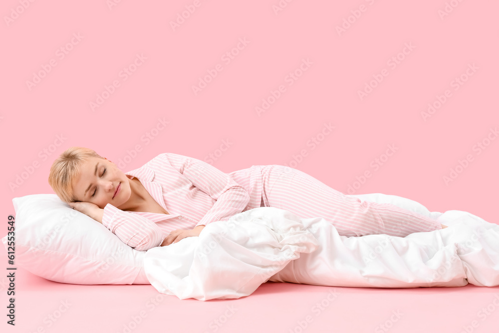 Young woman with pillow and soft blanket sleeping on pink background