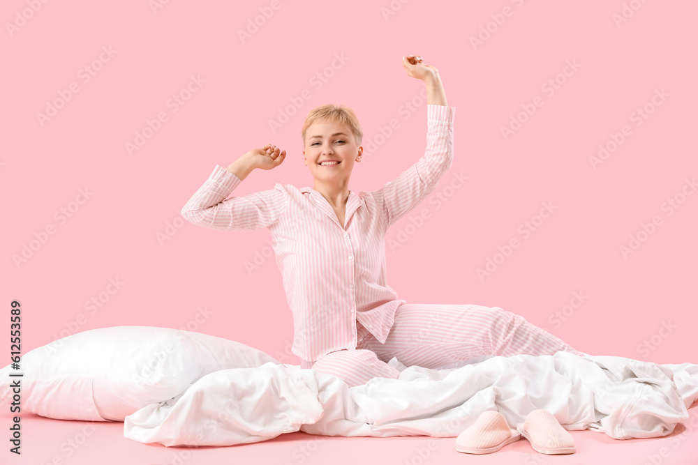 Awake young woman with soft blanket and pillow on pink background