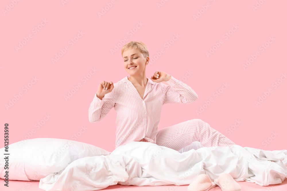 Awake young woman with soft blanket and pillow on pink background