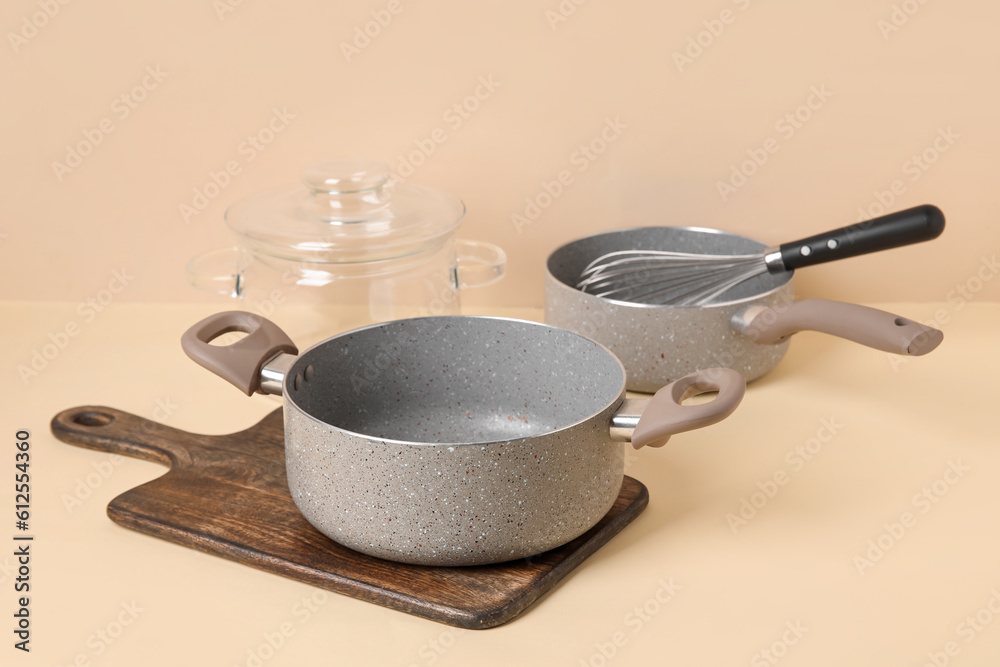 Cooking pots and whisk on beige background