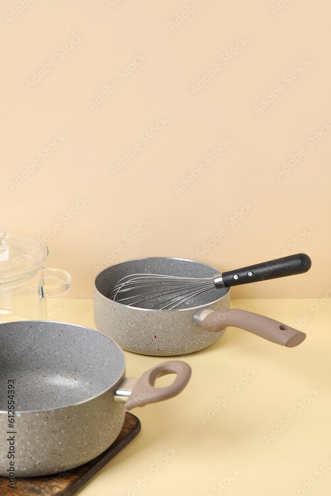 Cooking pots and whisk on beige background