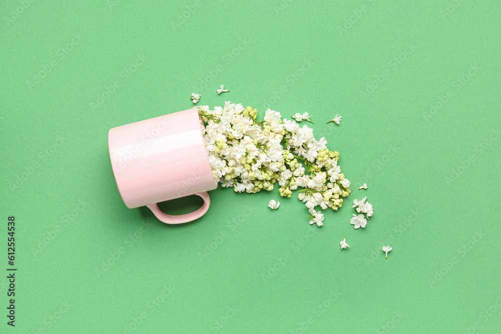 Overturned cup with white lilac flowers on green background