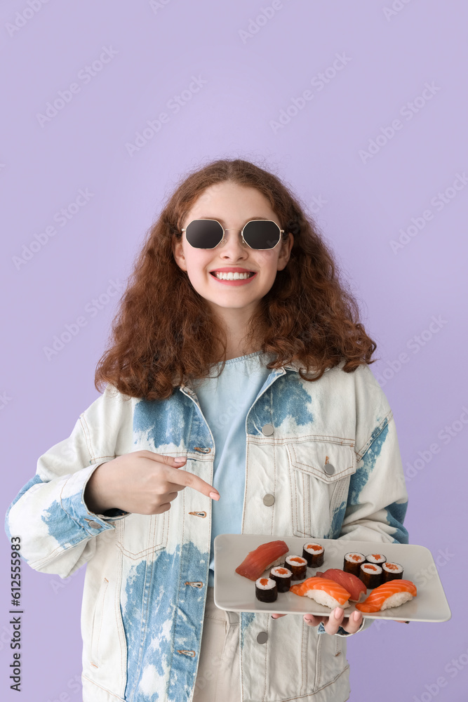 Young woman pointing at sushi on lilac background